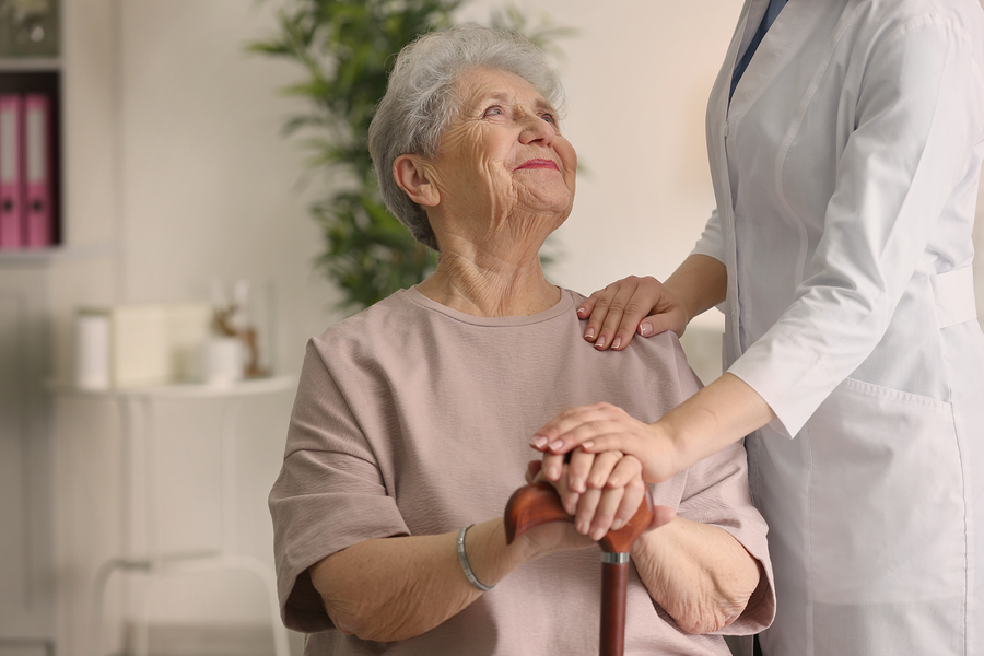 Elderly woman holding hands on walking stick and listening doctor in light room